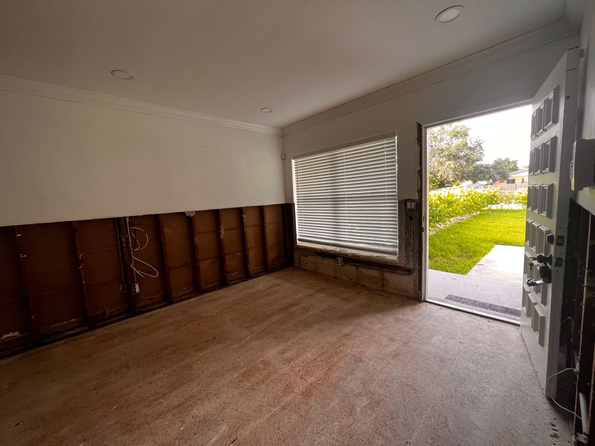 Empty room with wooden cabinets, open door, and bright view of a garden outside