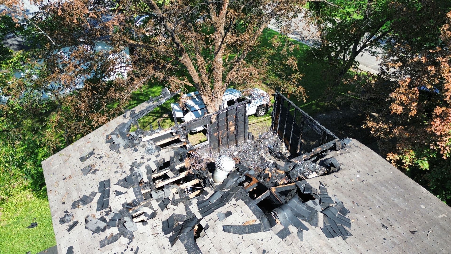 Burned roof with charred debris and soot marks among surrounding trees, seen from above