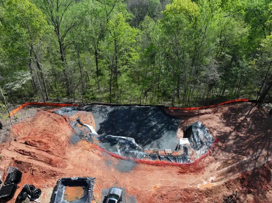 Construction site with black liner and orange soil beside a wooded area