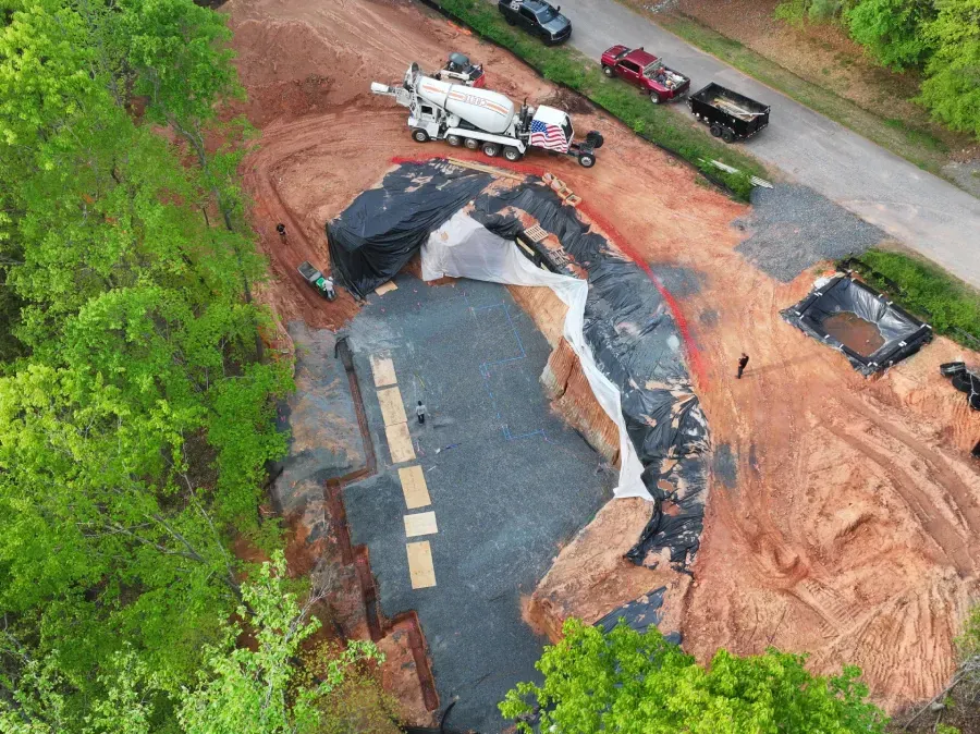 Aerial view of a washed-out road and collapsed ground beside trees, with vehicles parked nearby.