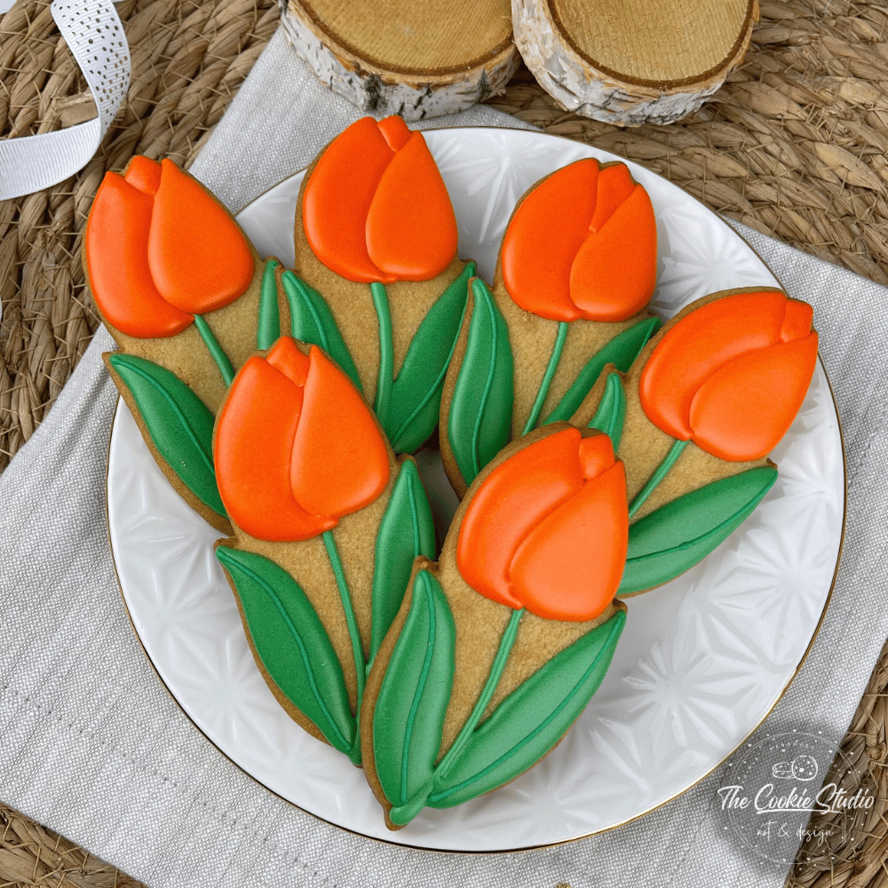 Een bord met oranje, tulpvormige koekjes met groene blaadjes, geplaatst op een wit bord en daarop een servet.