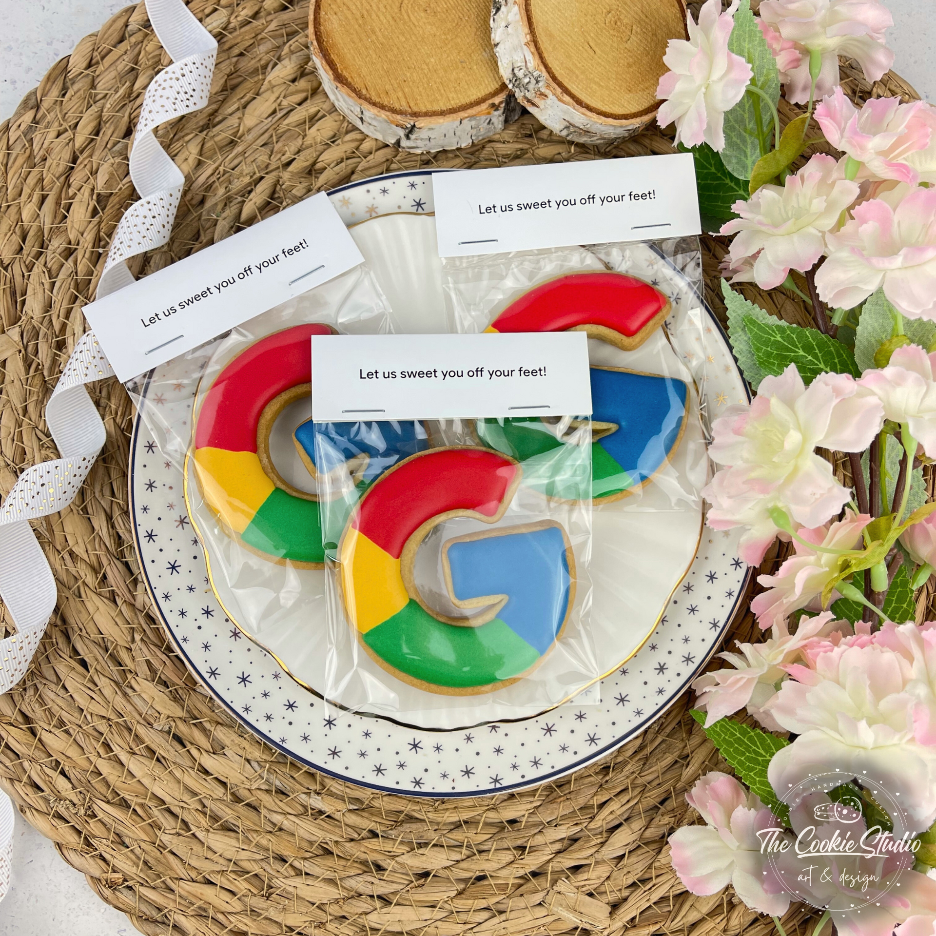 Koekjes met het Google-logo in een doorzichtige zak op een bord, omringd door bloemen en lint.
