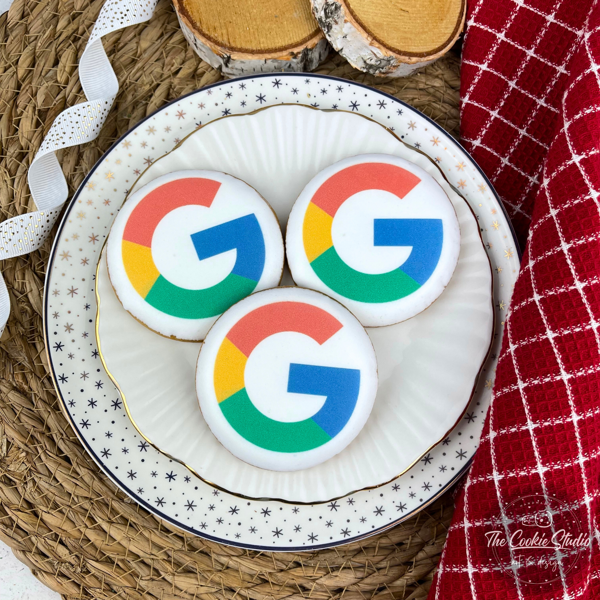 Drie met glazuur bedekte Google-logokoekjes op een versierd bord, met een rode servet en houten schijven op de achtergrond.
