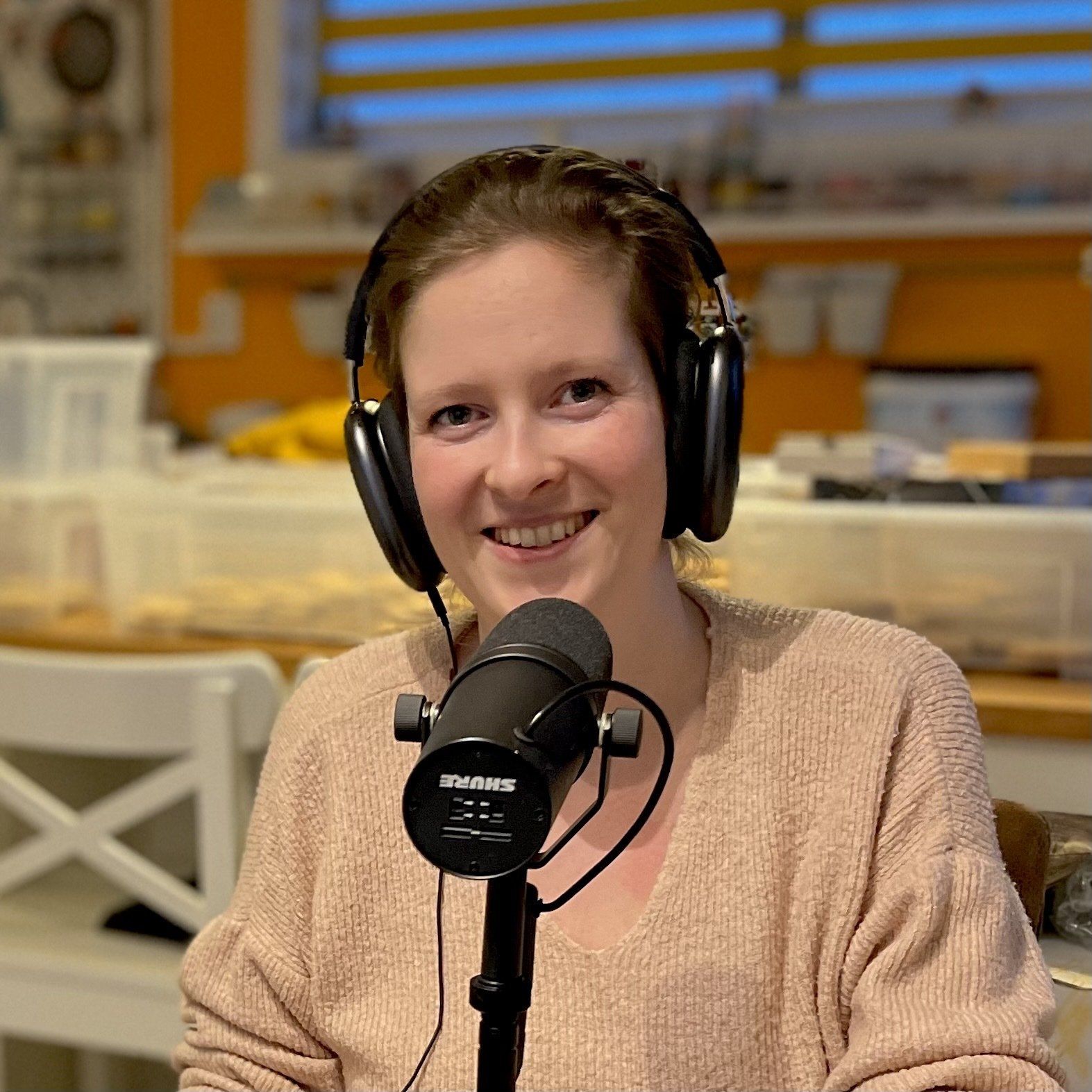 Vrouw met koptelefoon en microfoon, lachend, voor een wazige achtergrond.