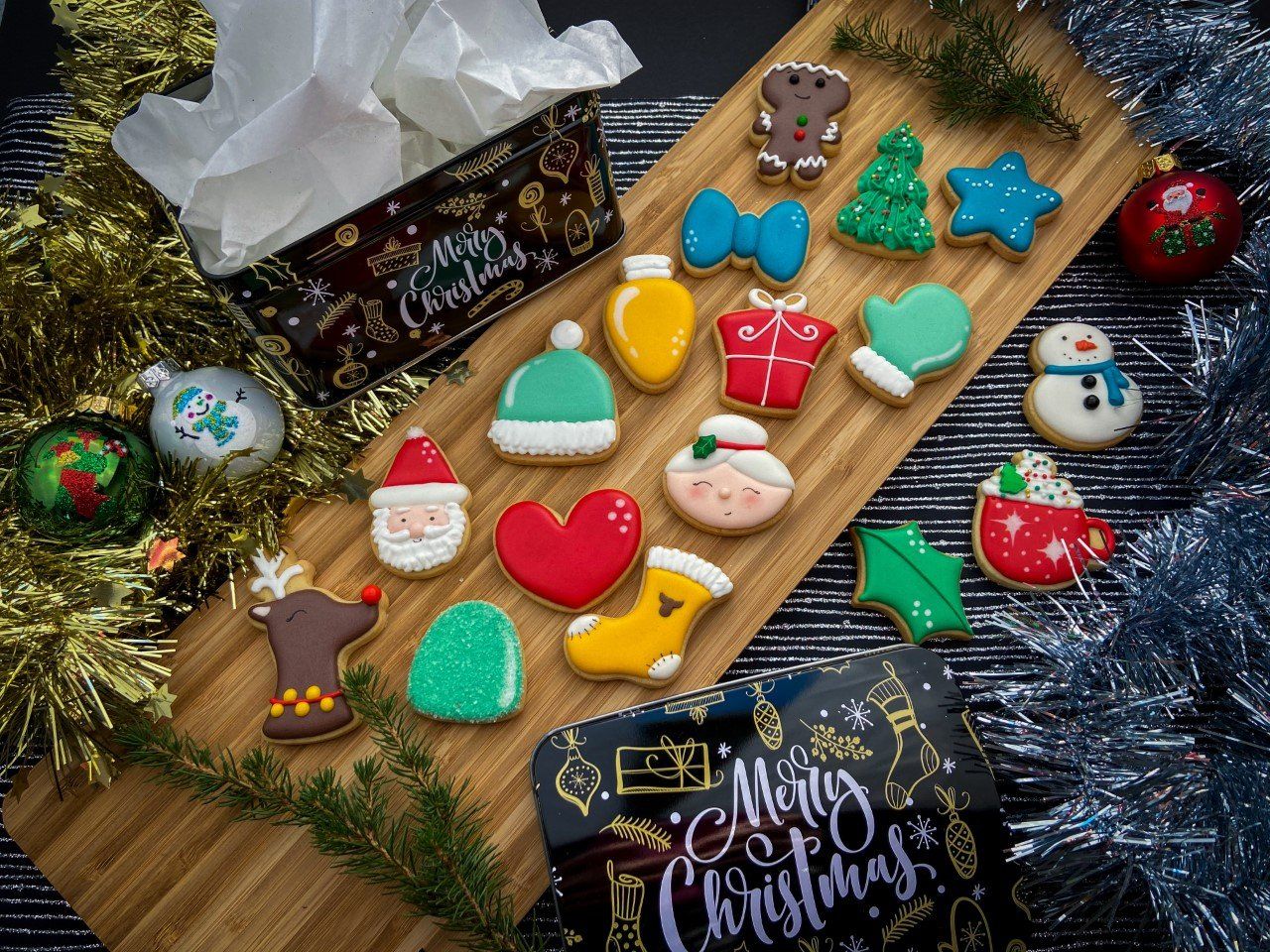 Kerstkoekjes op een houten plank, met een decoratieve doos, versieringen en een slinger.