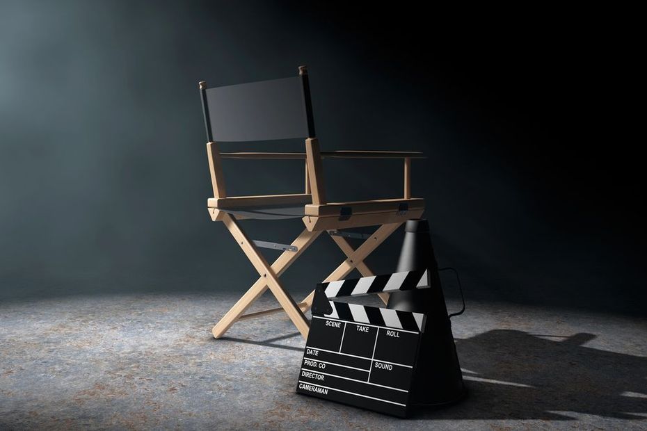 Una sedia da regista e un ciak cinematografico, sullo sfondo di un'ambientazione scura illuminata da faretti drammatici.