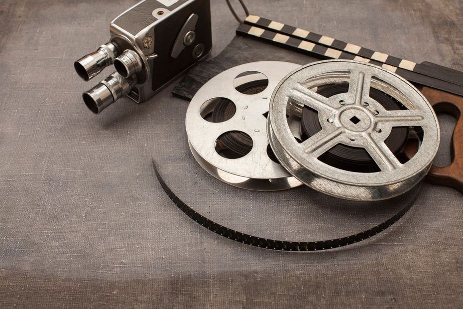 Cinepresa d'epoca, bobine di pellicola e ciak su uno sfondo grigio con texture.