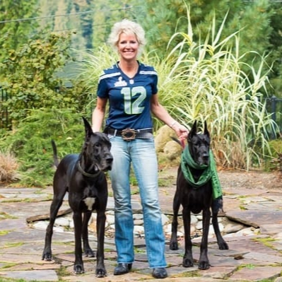Faith standing with her two fur babies, all decked out in Seahawks gear and ready to cheer on their team.