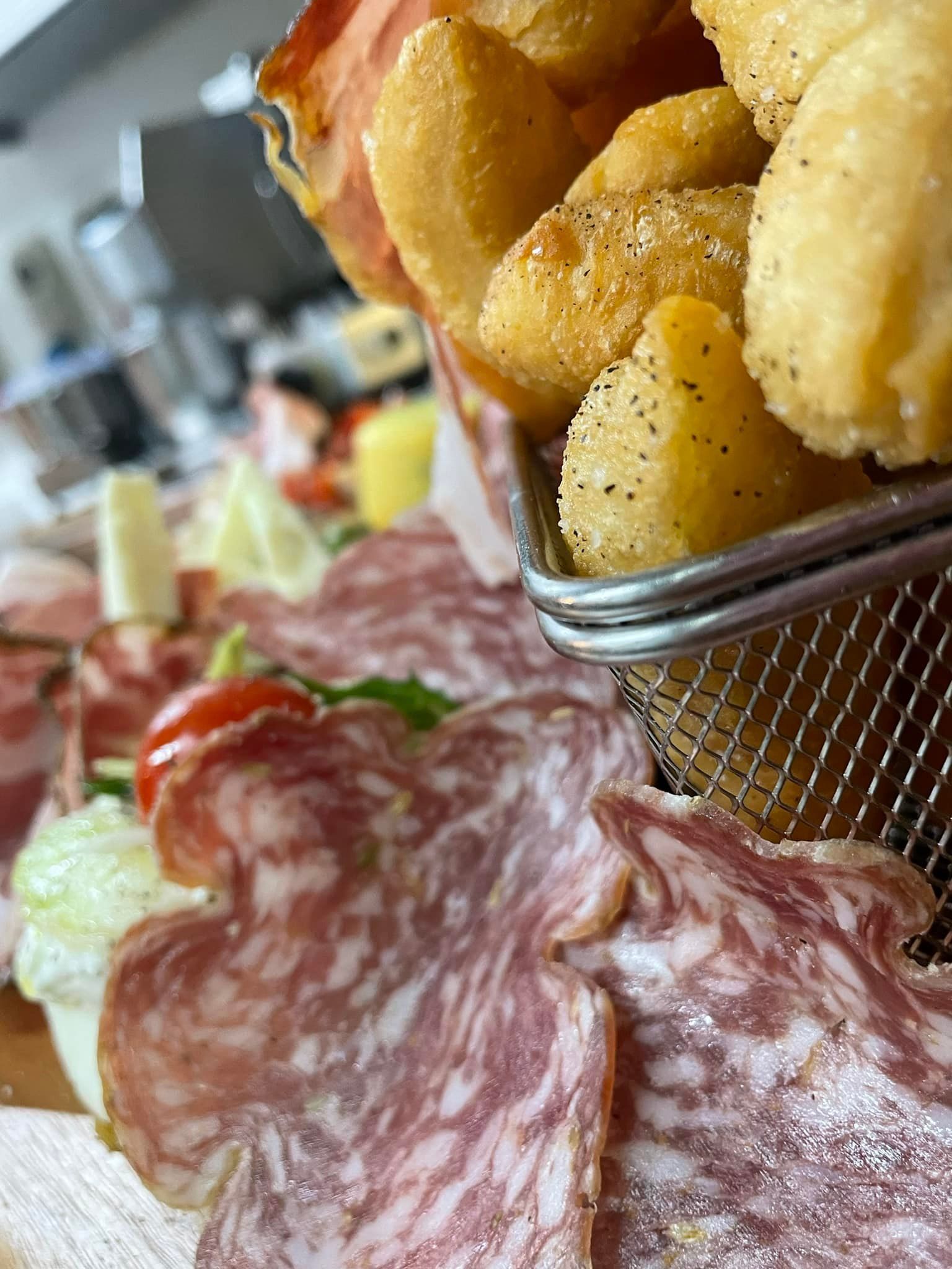Un cestino di patate fritte è posto sopra un piatto di carne e verdure.