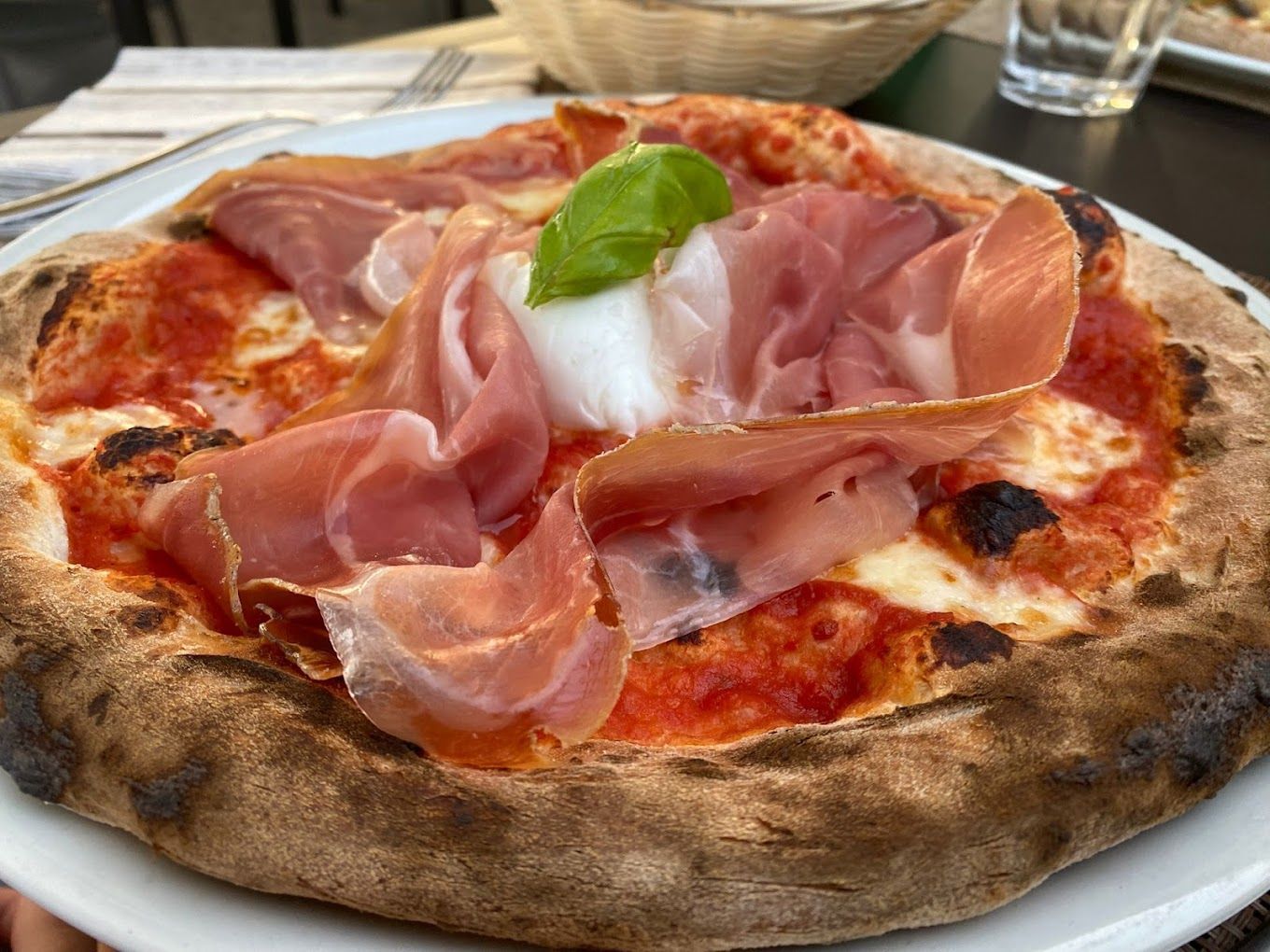 Una pizza con prosciutto, formaggio e basilico su un piatto bianco.