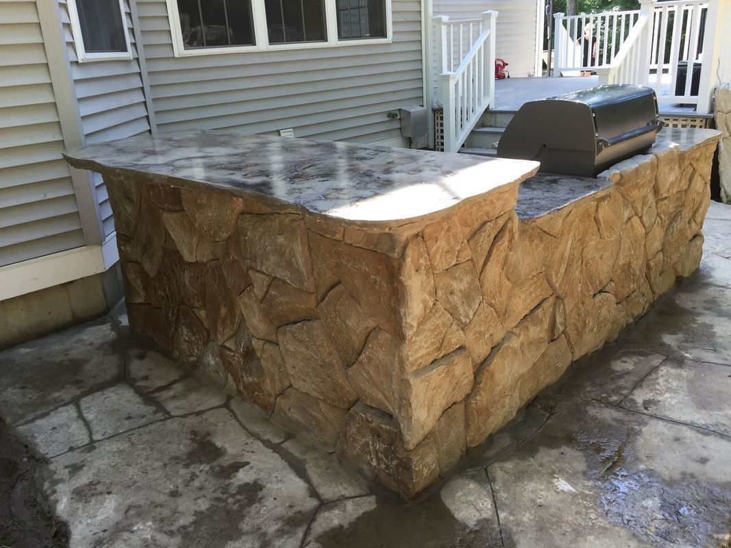 Outdoor stone kitchen island with a grill on a flagstone patio.