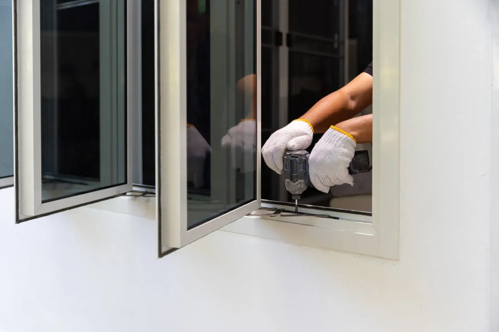 A person installing a window using a drill, wearing gloves.