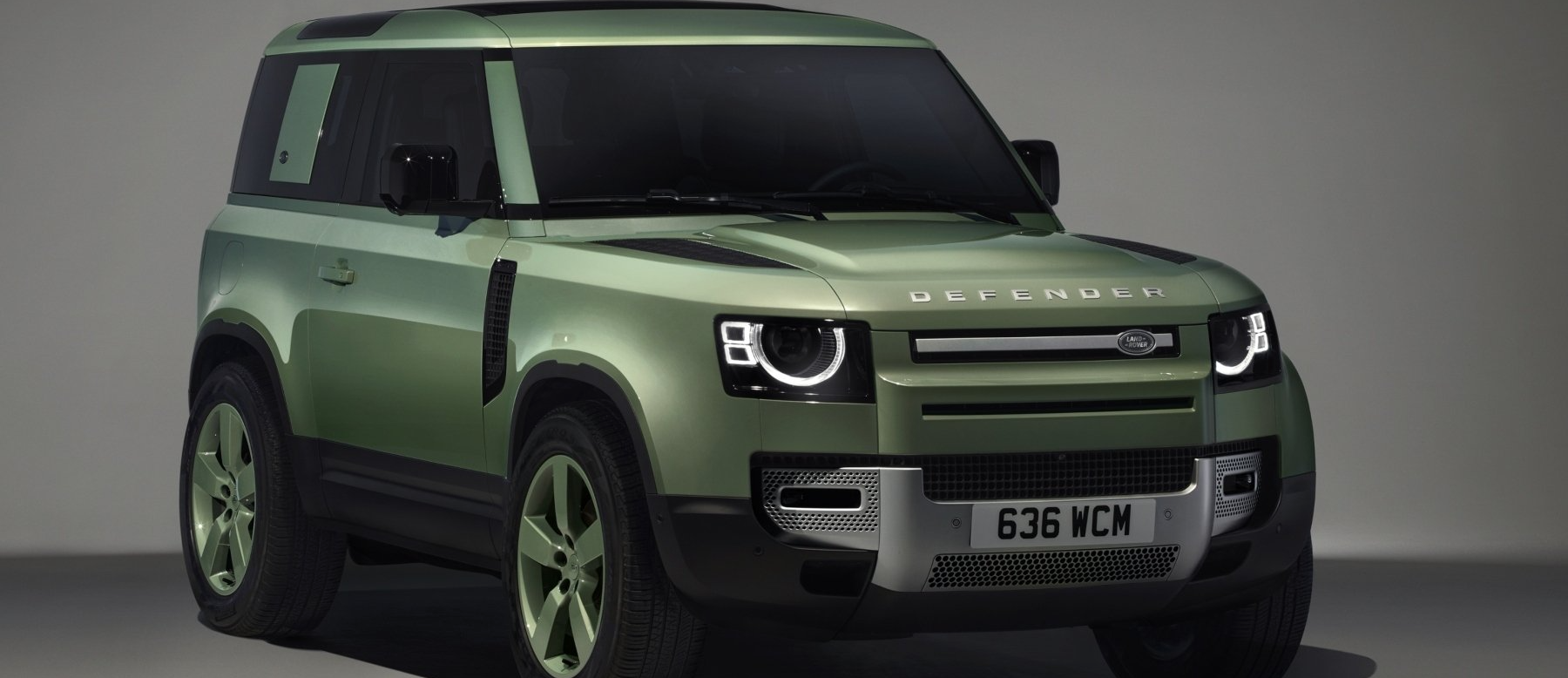 A green land rover defender is parked in front of a white wall.