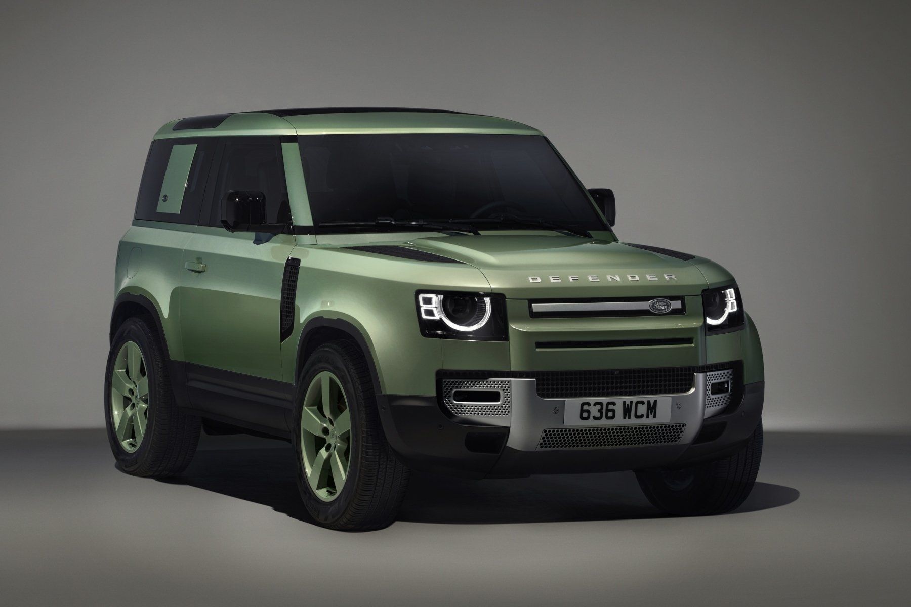 A green land rover defender is parked on a gray surface.
