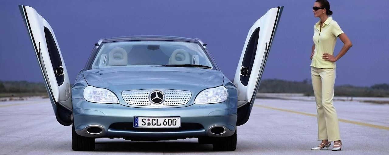 A woman stands in front of a blue mercedes with the doors open