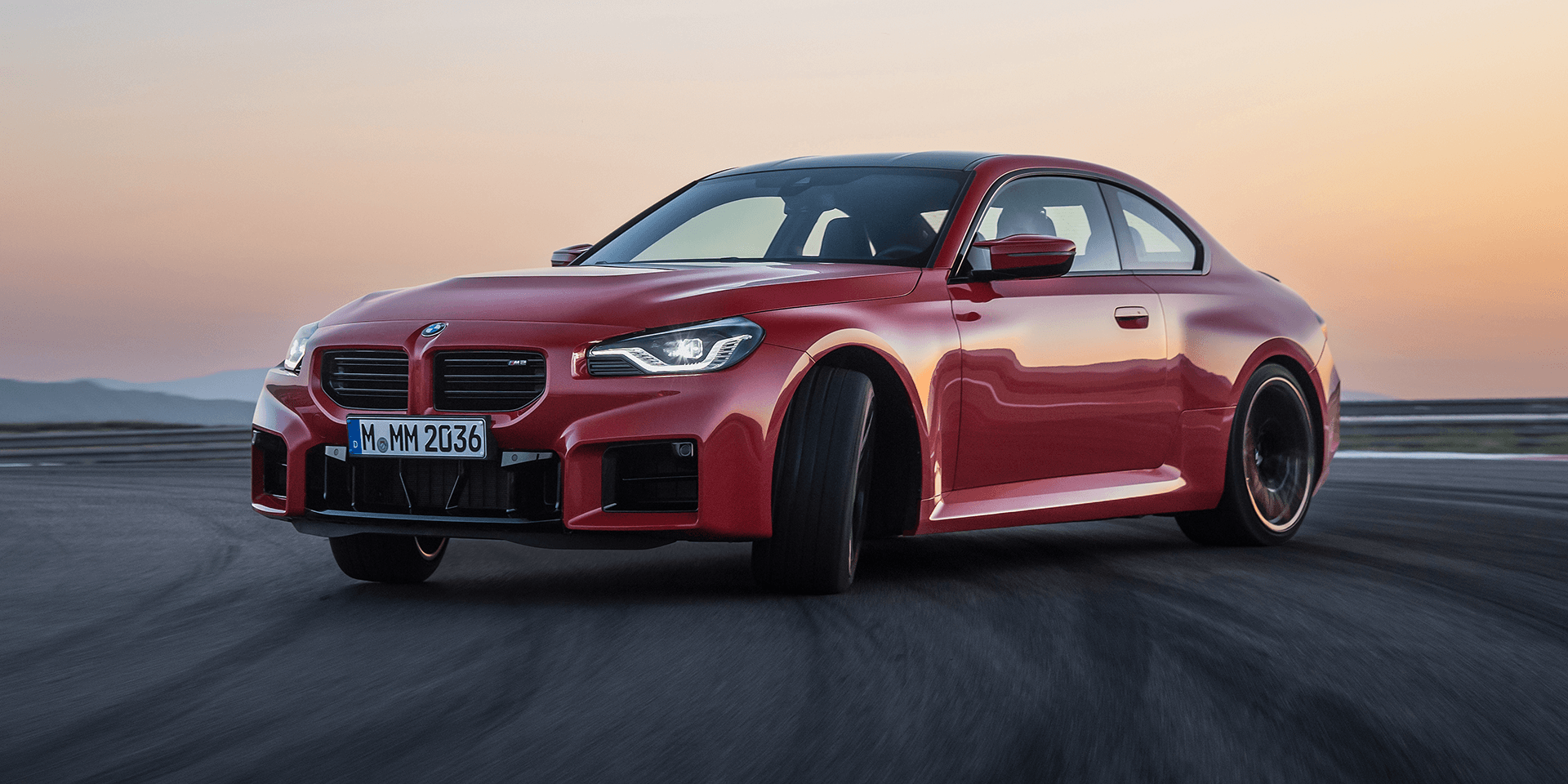 A red bmw m4 is driving down a road at sunset.