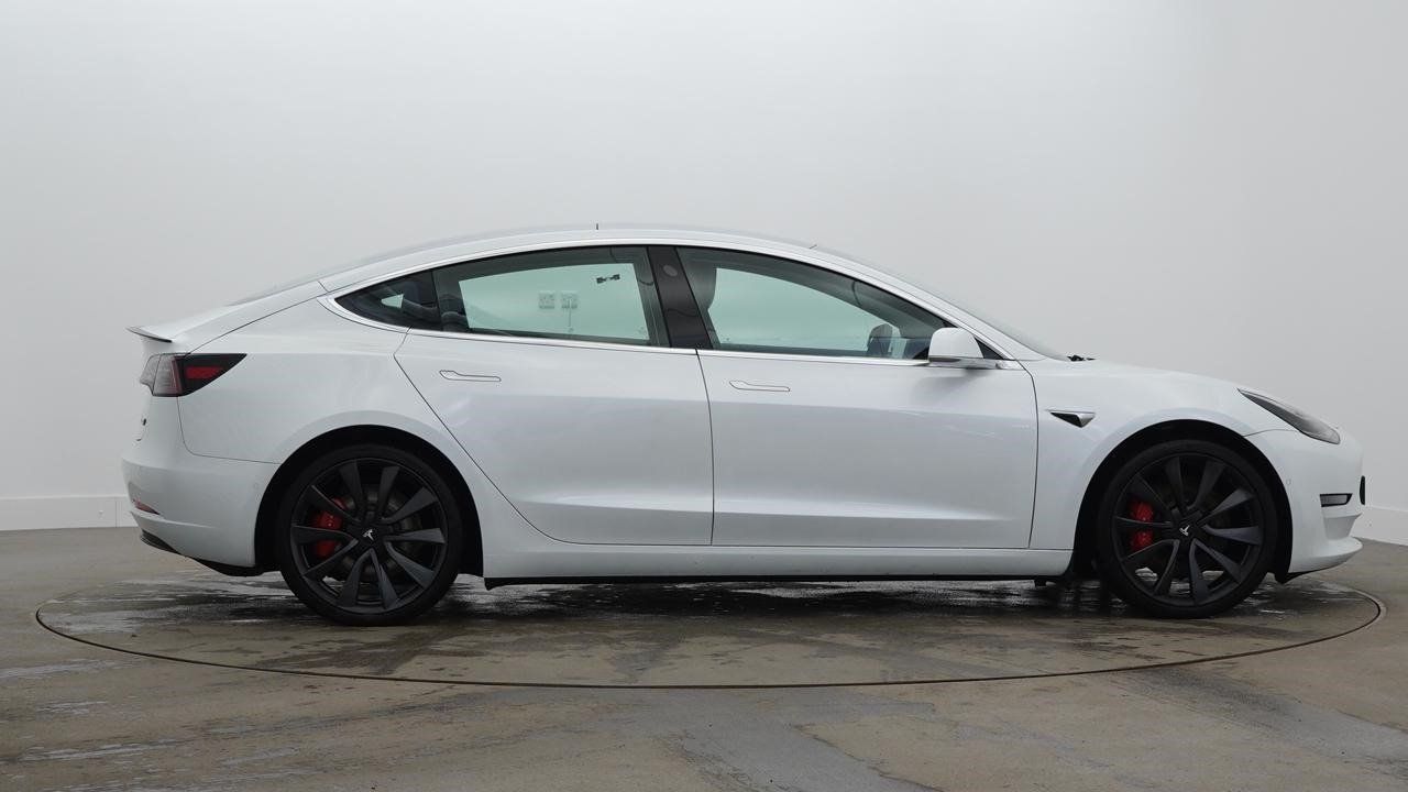 A white tesla model 3 is parked on a concrete floor.