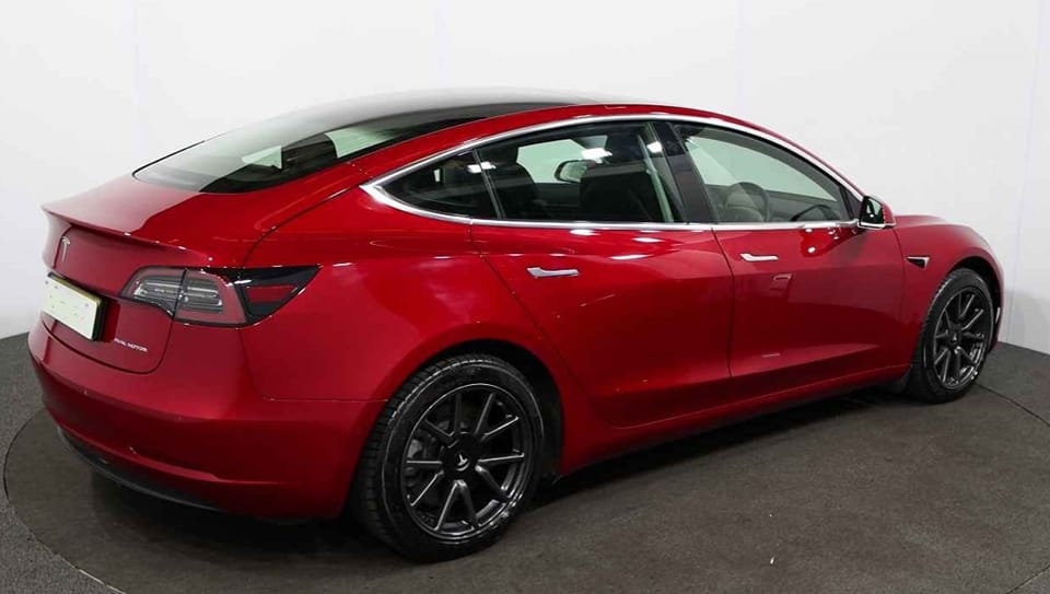 A red tesla model 3 is parked on a white surface.