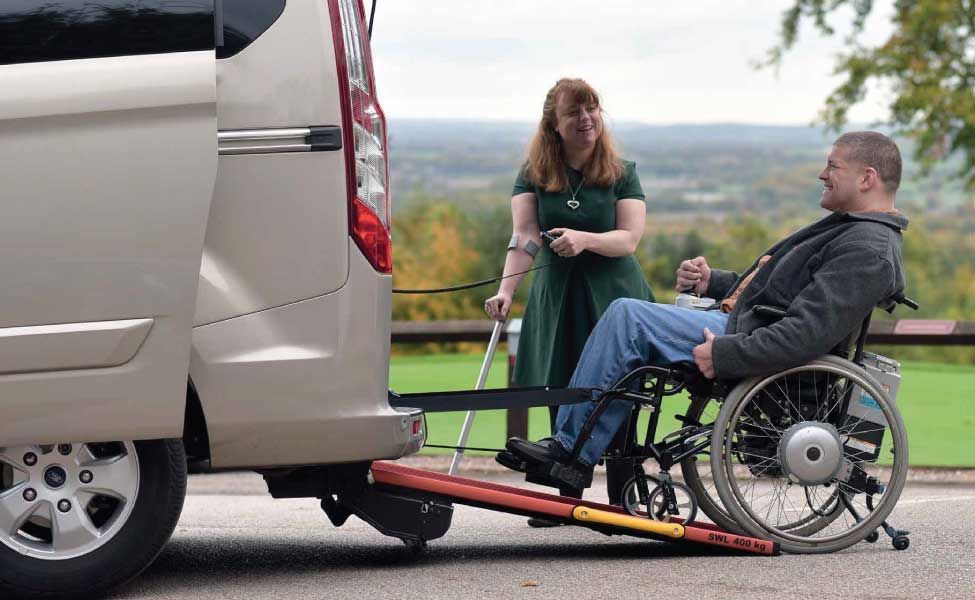 A woman is helping a man in a wheelchair get into a van.