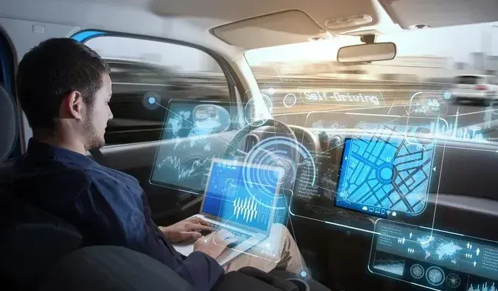 A man is sitting in a self driving car using a laptop computer.