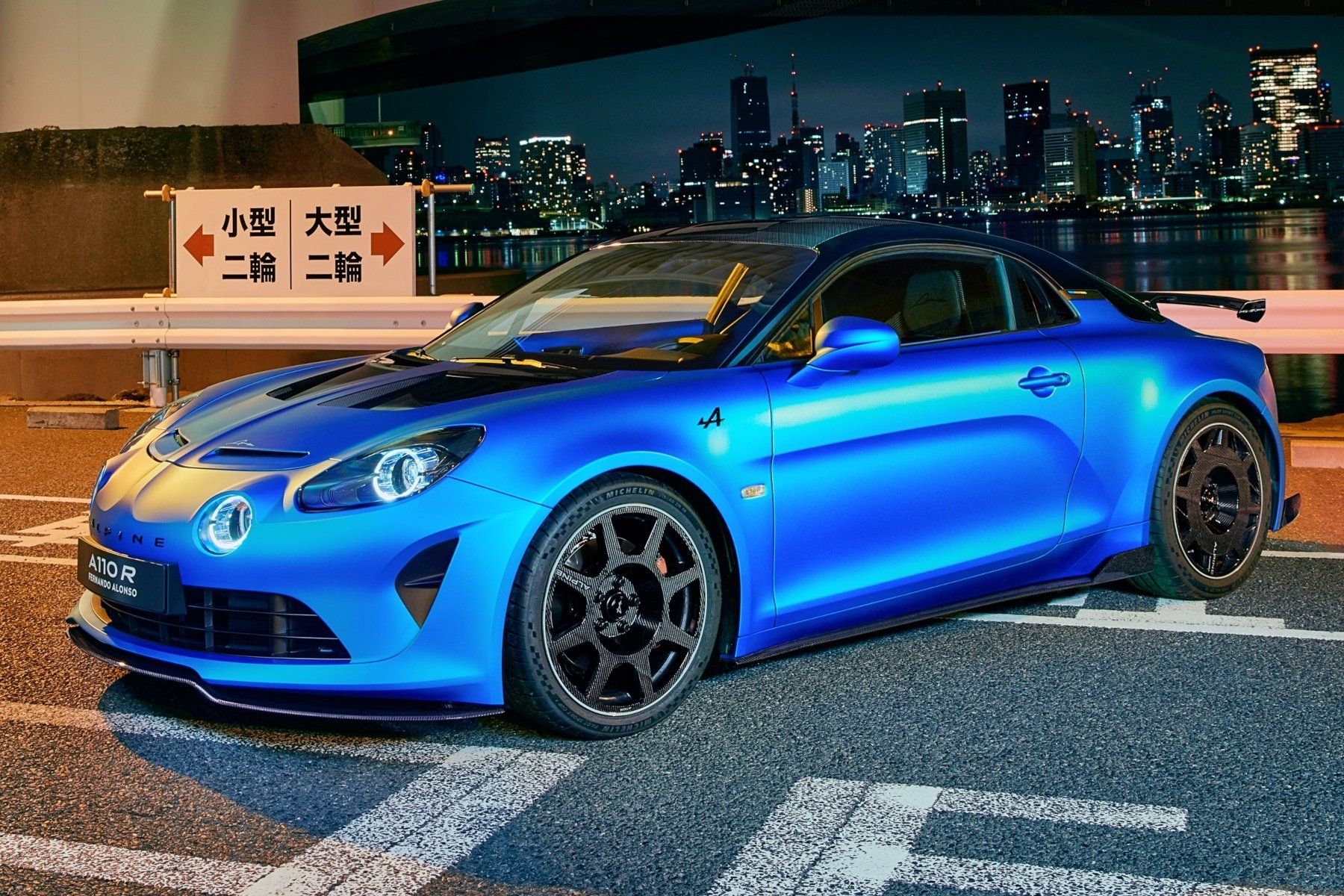 A blue sports car is parked on the side of a road at night.
