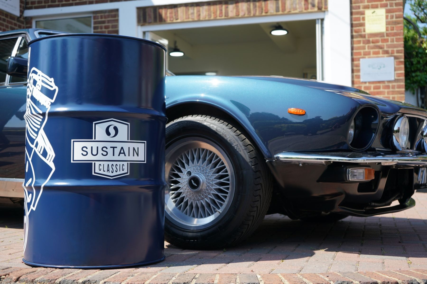A blue car is parked next to a blue barrel that says sustain