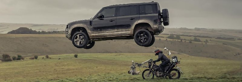 A man is riding a motorcycle next to a car that is flying through the air.