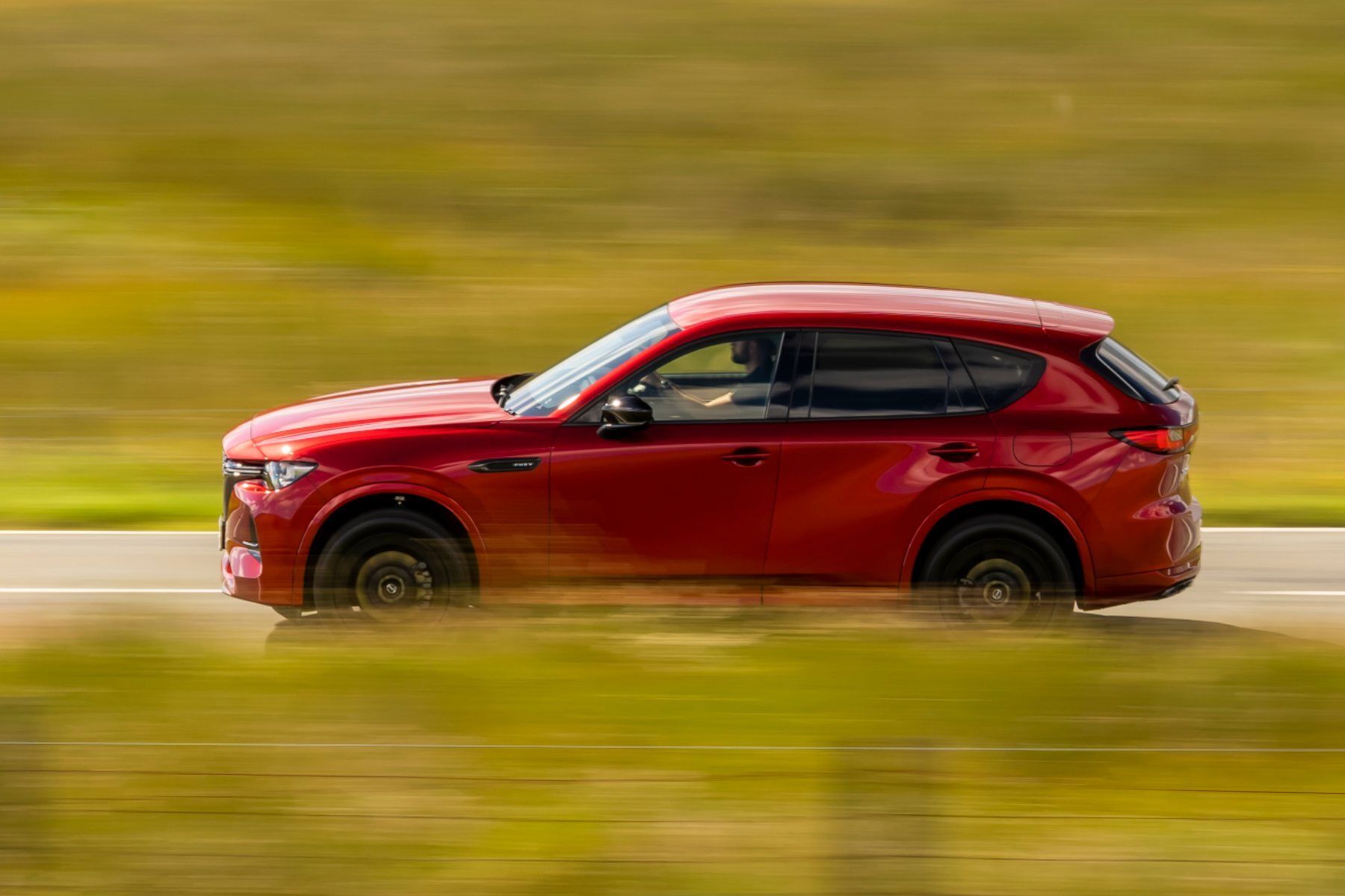 A red car is driving down a road in a field.
