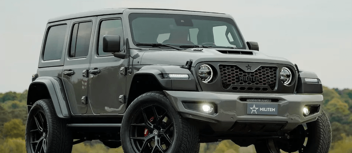 A jeep is parked in a field with trees in the background.
