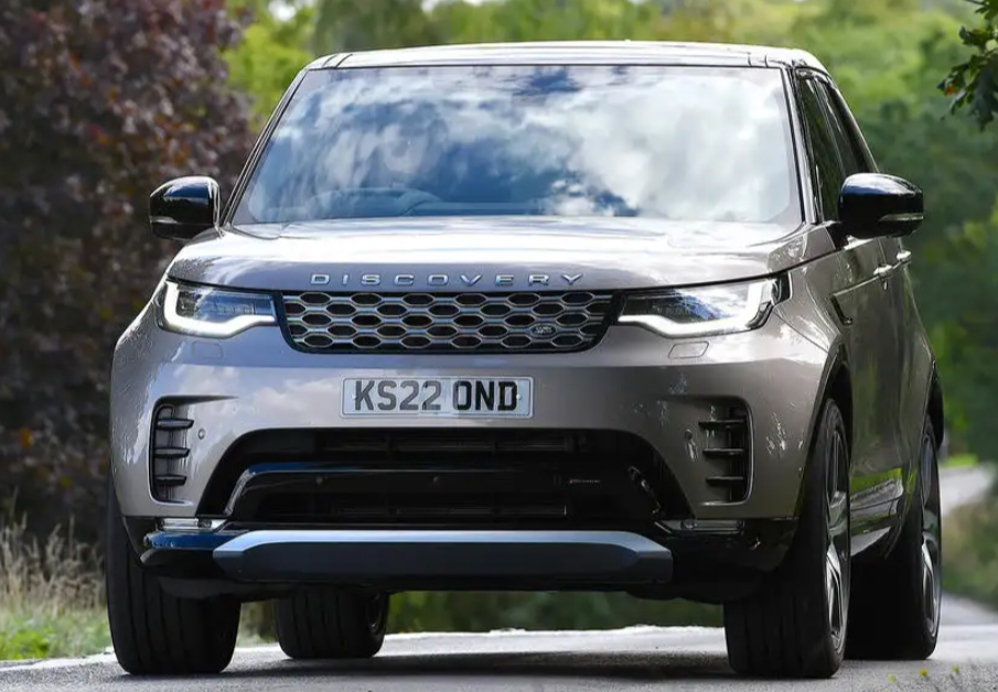 A silver land rover discovery is driving down a country road.