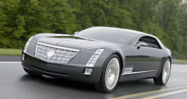 A gray car is driving down a road next to trees.
