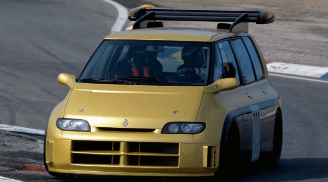 A yellow renault car is driving down a road