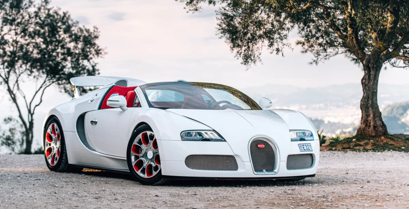 A white bugatti veyron is parked next to a tree on a gravel road.