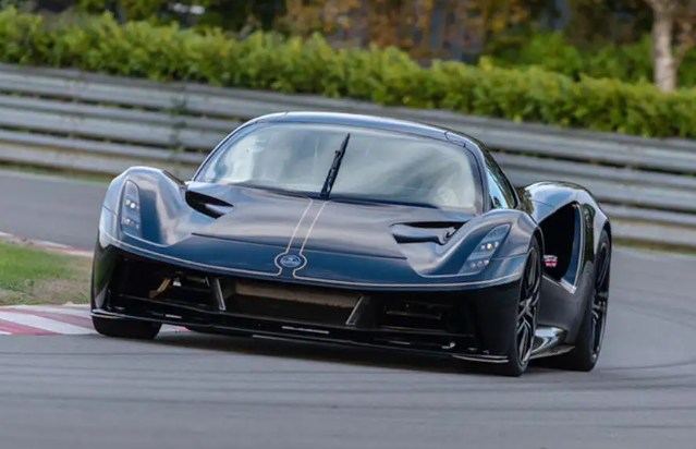 A black sports car is driving down a race track.
