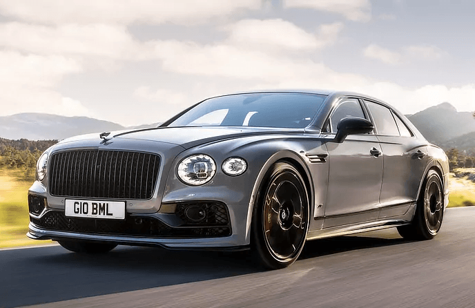 A bentley flying spur is driving down a road with mountains in the background.