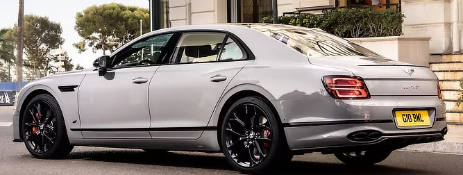 A silver bentley flying spur is parked in front of a building.