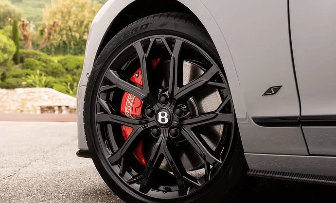 A close up of a bentley with black wheels and red brake calipers.