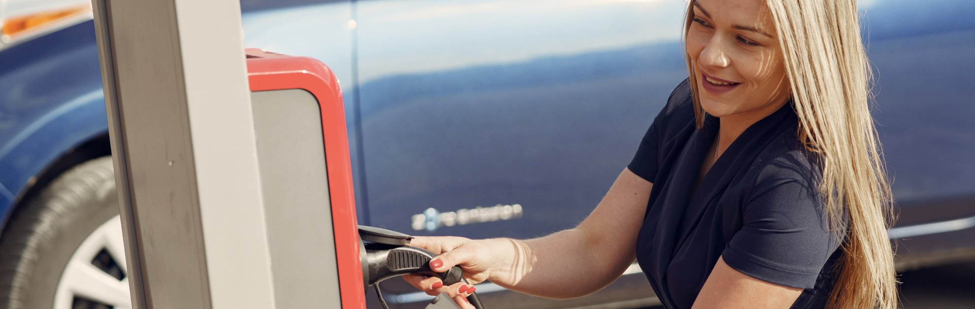 A woman is pumping gas into her car at a gas station.