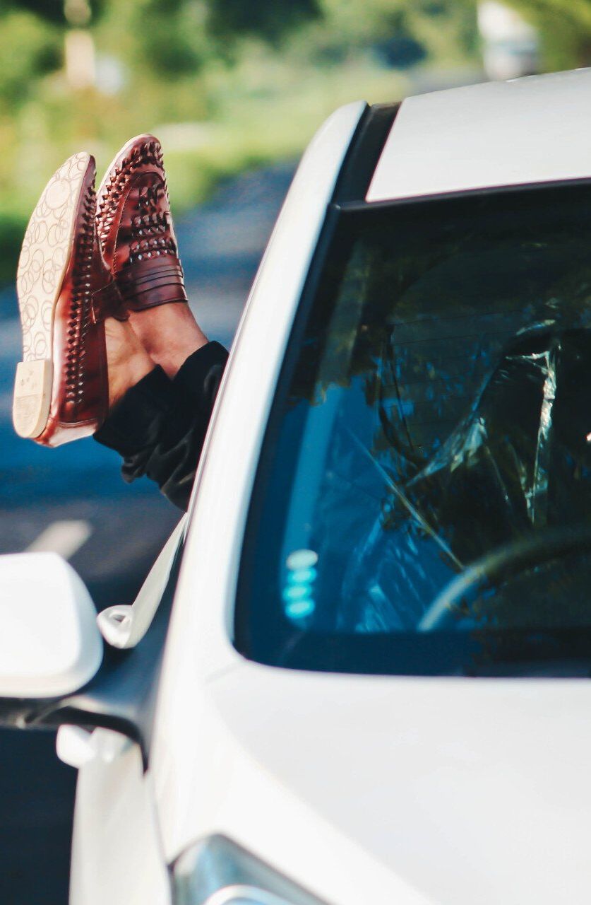 A person 's feet are sticking out of the window of a car.
