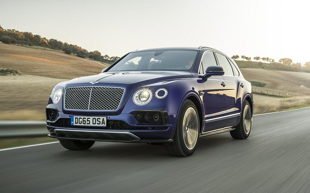 A blue bentley is driving down a road.