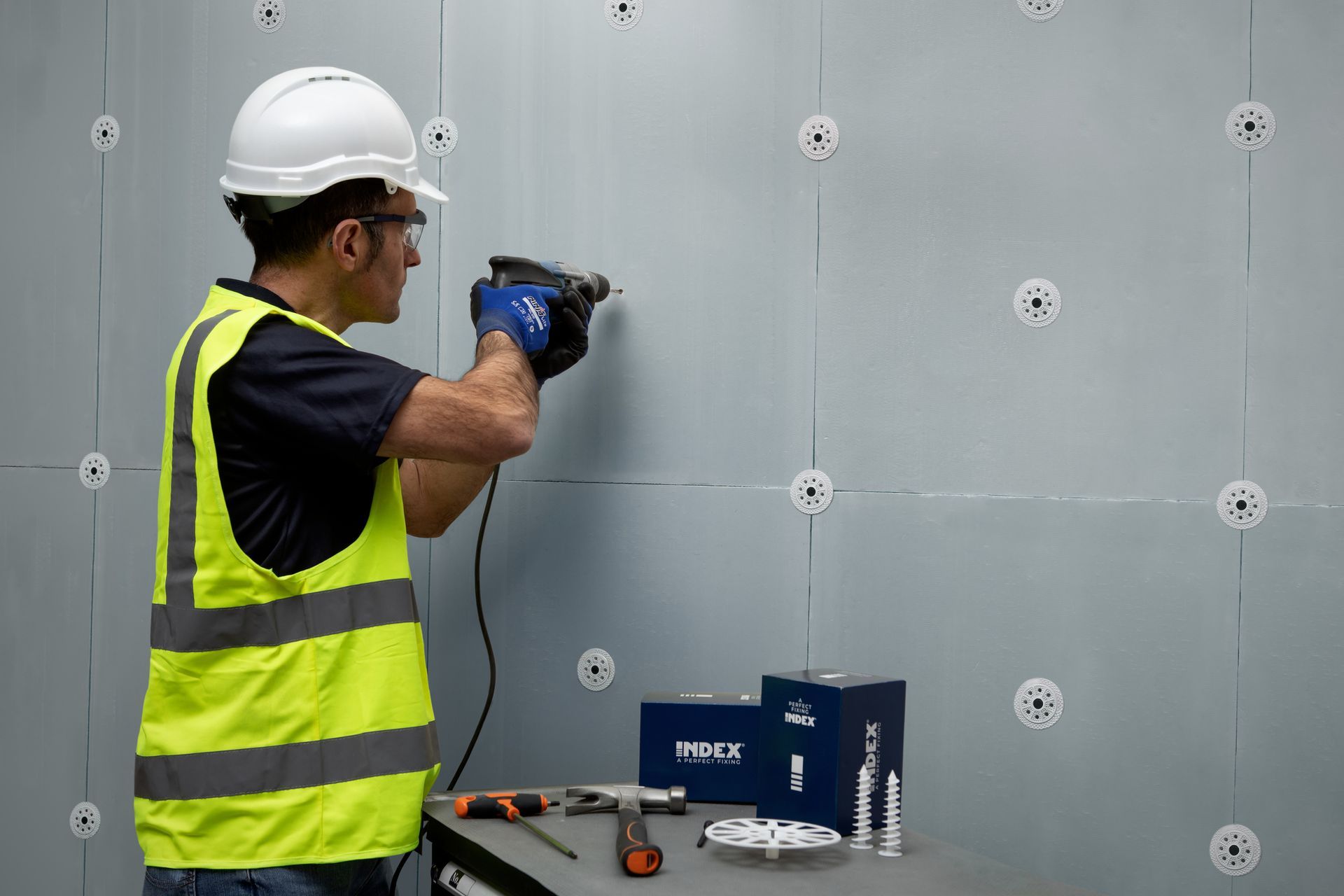 Un uomo con un elmetto sta usando un trapano su un muro.