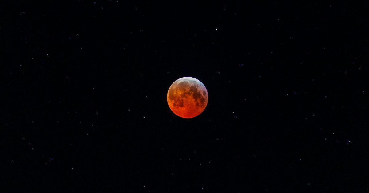Una luna de color rojo anaranjado sobre un cielo oscuro y estrellado.