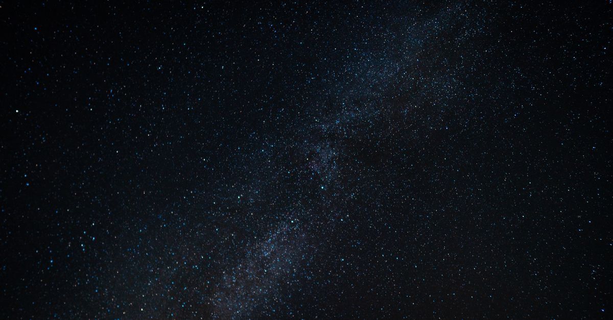 Un cielo estrellado con la Vía Láctea extendiéndose en diagonal sobre un horizonte oscuro.