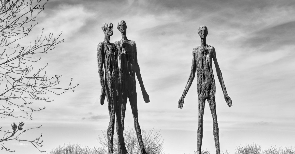 Dos figuras oscuras, altas y esbeltas, de pie en un campo baldío bajo un cielo nublado