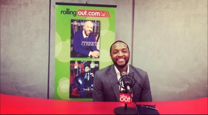 Man in a suit smiles, speaking into a microphone at a 