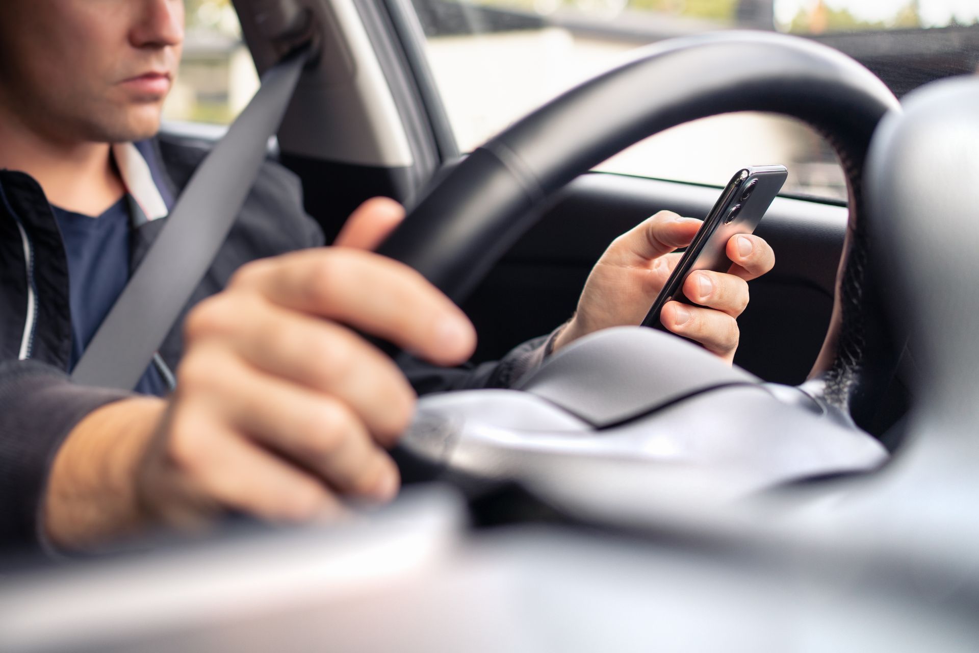 A distracted driver typing on his cellphone by his steering wheel. A distracted driver typing on his cellphone by his steering wheel.