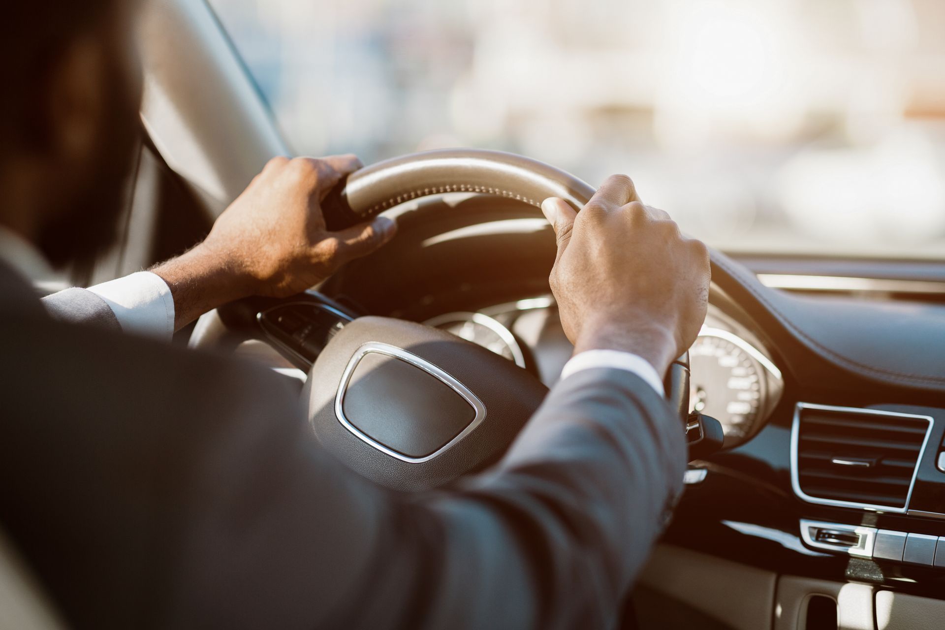 Unrecognizable man in a suit driving a car during the day. 