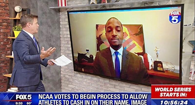 A news anchor in a suit interviews a man on a large screen discussing NCAA athletes' name, image, and likeness.