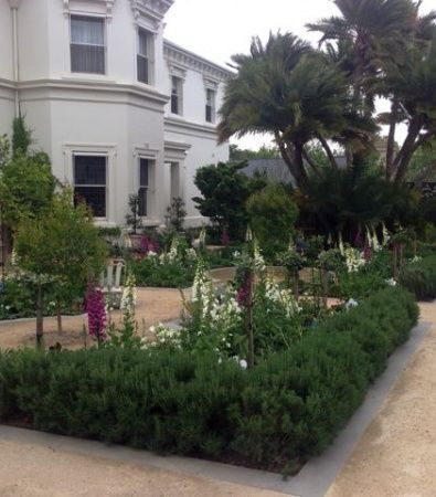 White villa with a landscaped garden, palm trees, and a gravel path beside trimmed hedges.