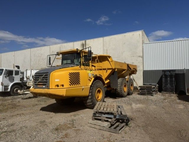 Yellow articulated dump truck parked in an industrial yard beside a warehouse